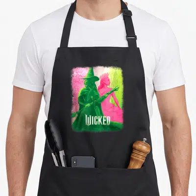 Tablier de cuisine noir avec illustration colorée d'Elphaba et Glinda du film Wicked sur fond dégradé.