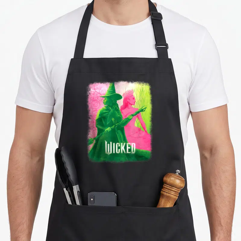 Tablier de cuisine noir avec illustration colorée d'Elphaba et Glinda du film Wicked sur fond dégradé.