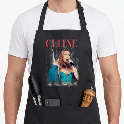 Tablier de cuisine noir avec une illustration de Celine Dion en robe turquoise et texte rose ainsi que blanc.