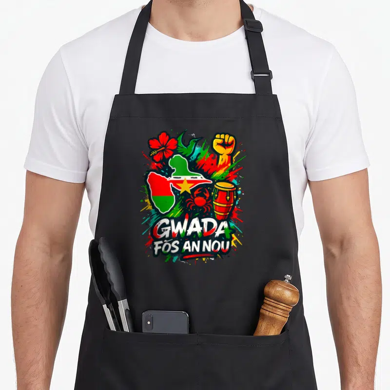 Tablier de cuisine noir avec illustration colorée Gwada Fós An Nou En Couleur incluant hibiscus, colibri et tambour.