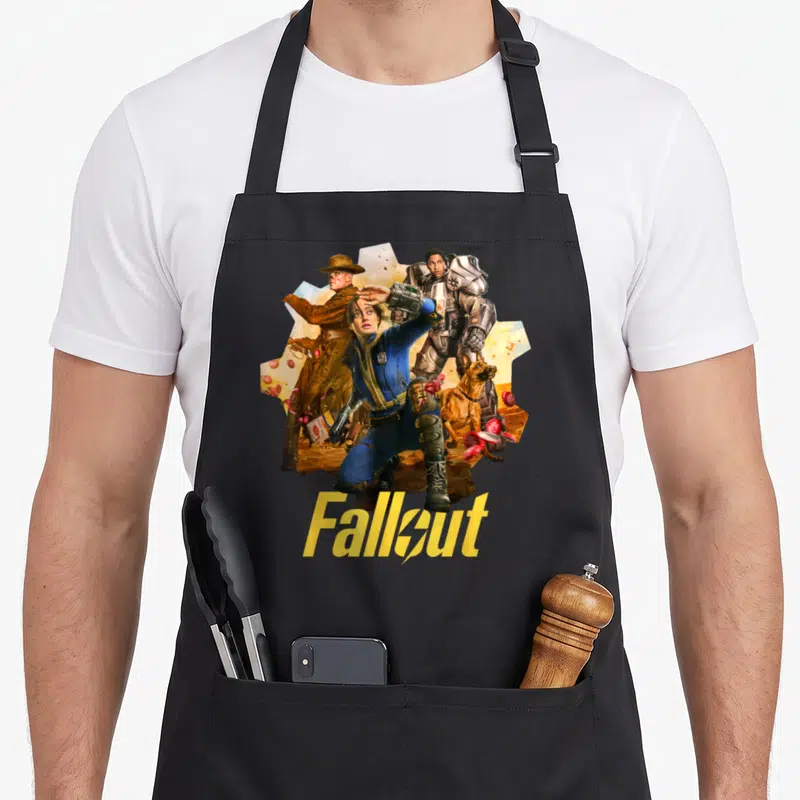 Tablier de cuisine noir avec illustration colorée de trois protagonistes et un chien accompagnés du titre Fallout en typographie distinctive.