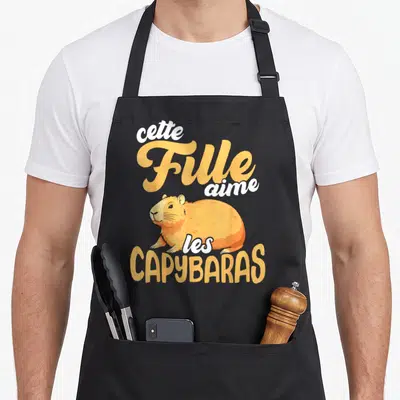 Tablier de cuisine noir avec illustration d'un capybara orange et le texte cette Fille aime les CAPYBARAS en typographie stylisée.