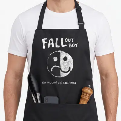 Tablier de cuisine noir avec le texte Fall Out Boy, un visage souriant et triste, et So Much For Stardust imprimé en blanc.