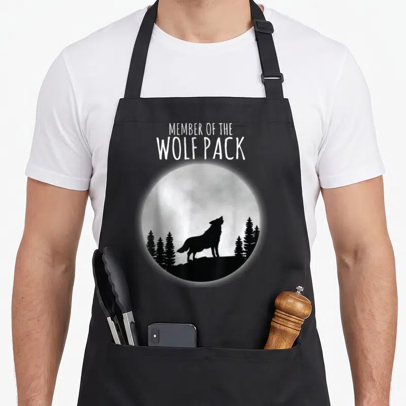 Tablier de cuisine noir avec silhouette de loup hurlant sous une lune et texte member of the wolf pack