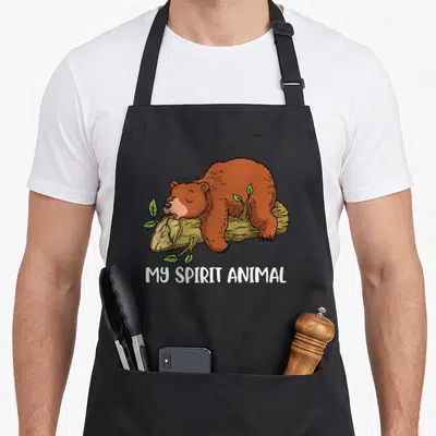 Tablier de cuisine noir avec illustration d'un ours grizzly dormant sur une bûche et le texte My Spirit Animal en blanc.