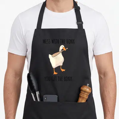 Tablier de cuisine noir avec un oiseau blanc tenant une baguette et du texte humoristique imprimé au centre.