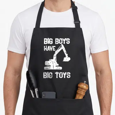 Tablier de cuisine noir avec inscription Big Boys Have Big Toys et silhouette de pelleteuse blanche au centre.