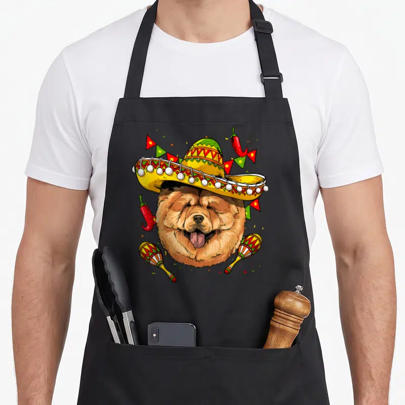Tablier de cuisine noir avec un Chow Chow portant un sombrero mexicain jaune et des maracas colorées.