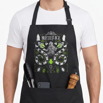 Tablier de cuisine noir avec illustration Beetlejuice, deux vers gris et verts, trident et scarabée lime au centre.