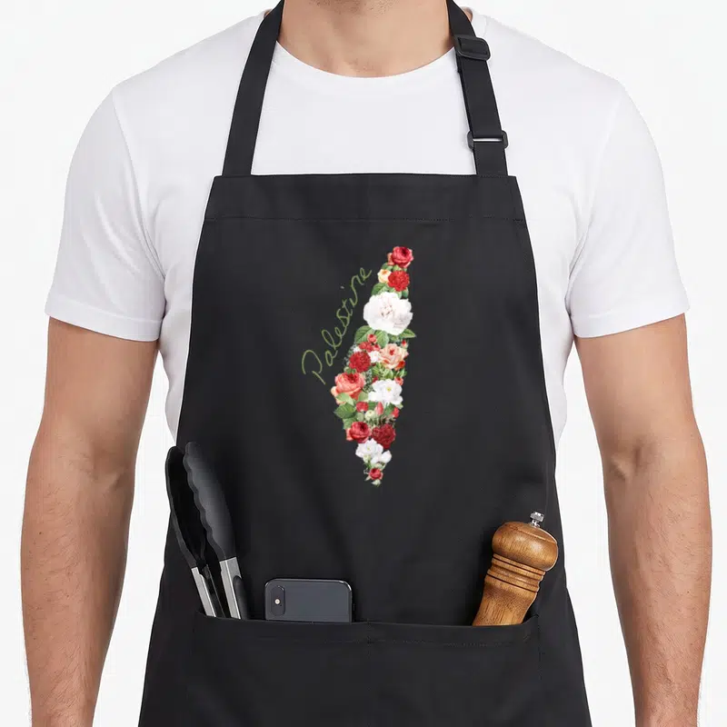 Tablier de cuisine noir avec une carte de Palestine décorée de fleurs roses, rouges et blanches ainsi que du texte J'aime la Palestine Ma Patrie.