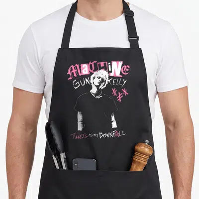 Tablier de cuisine noir avec le portrait de Machine Gun Kelly et des textes roses et blancs.
