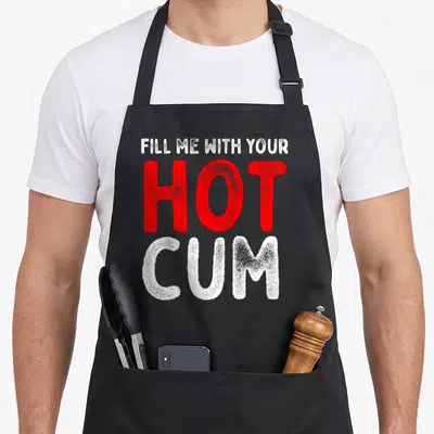 Tablier de cuisine noir avec inscription Fill Me With Your Hot Cum en lettres rouges et blanches texturées.