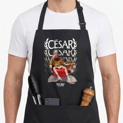 Tablier de cuisine noir avec César assis sur un trône rouge et doré, coiffé d'une couronne de laurier verte.