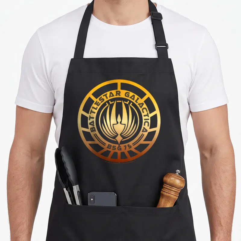 Tablier de cuisine noir avec le logo circulaire doré Battlestar Galactica BSG 75 imprimé au centre.