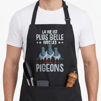 Tablier de cuisine noir avec trois pigeons bleus et le texte La Vie Est Plus Belle avec les Pigeons imprimé en blanc.