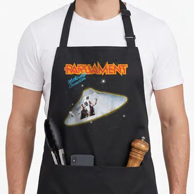 Tablier de cuisine noir avec illustration du vaisseau Mothership Connection et du texte Parliament en orange.