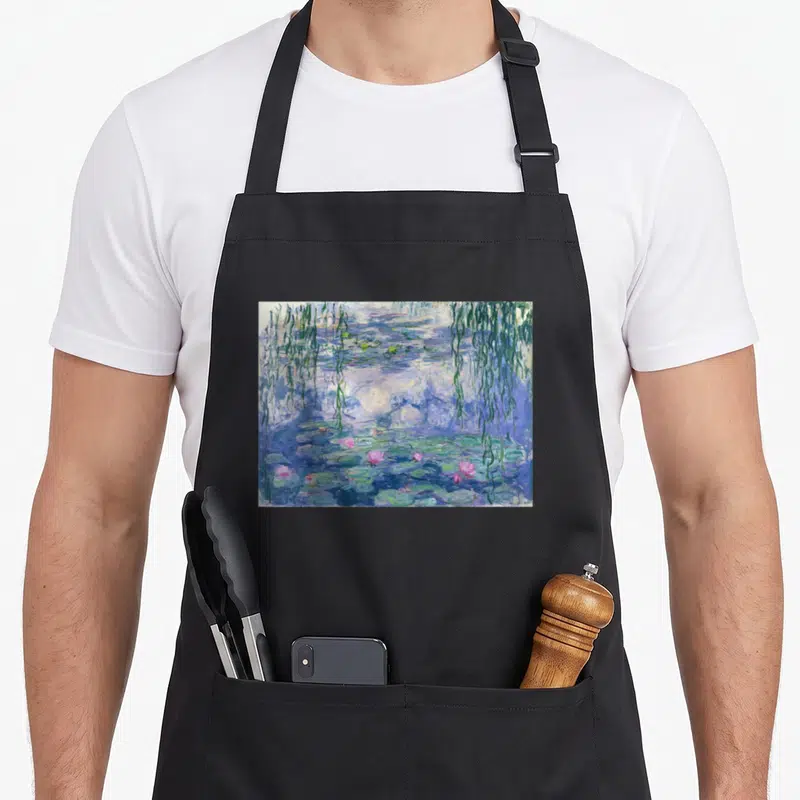 Tablier de cuisine noir avec une reproduction impressionniste de nénuphars roses et de saules pleureurs sur un plan d'eau bleu.