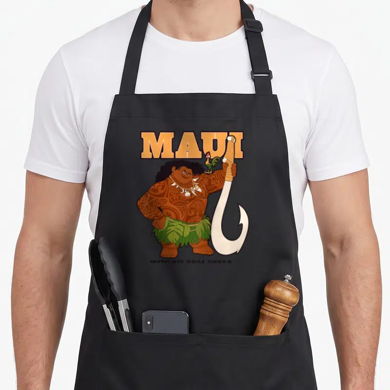 Tablier de cuisine noir avec illustration colorée de Maui tenant un grand crochet blanc et le texte Maui en orange au-dessus.