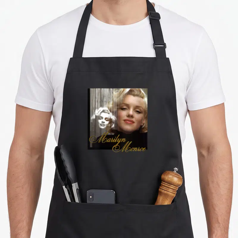 Tablier de cuisine noir avec portrait de Marilyn Monroe et signature dorée stylisée sur le devant.