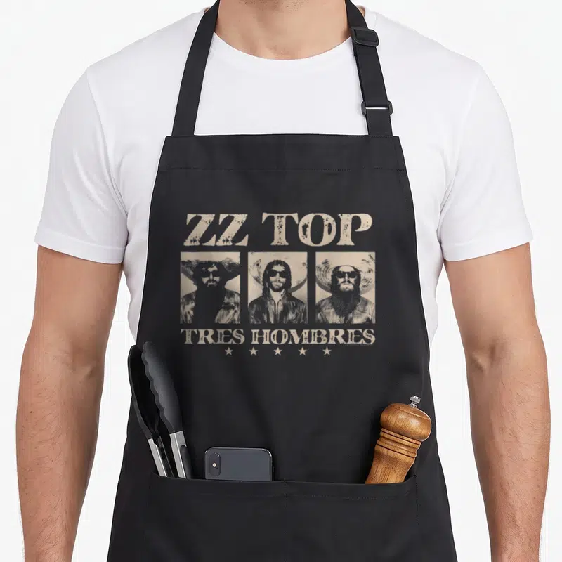 Tablier de cuisine noir avec l'inscription ZZ Top Tres Hombres et trois portraits de musiciens aux barbes et lunettes de soleil.