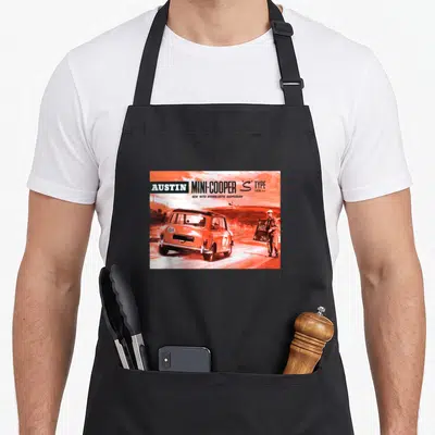 Tablier de cuisine noir avec illustration orange d'une Austin Mini Cooper S Type 1275 en course et un homme tenant un panneau.