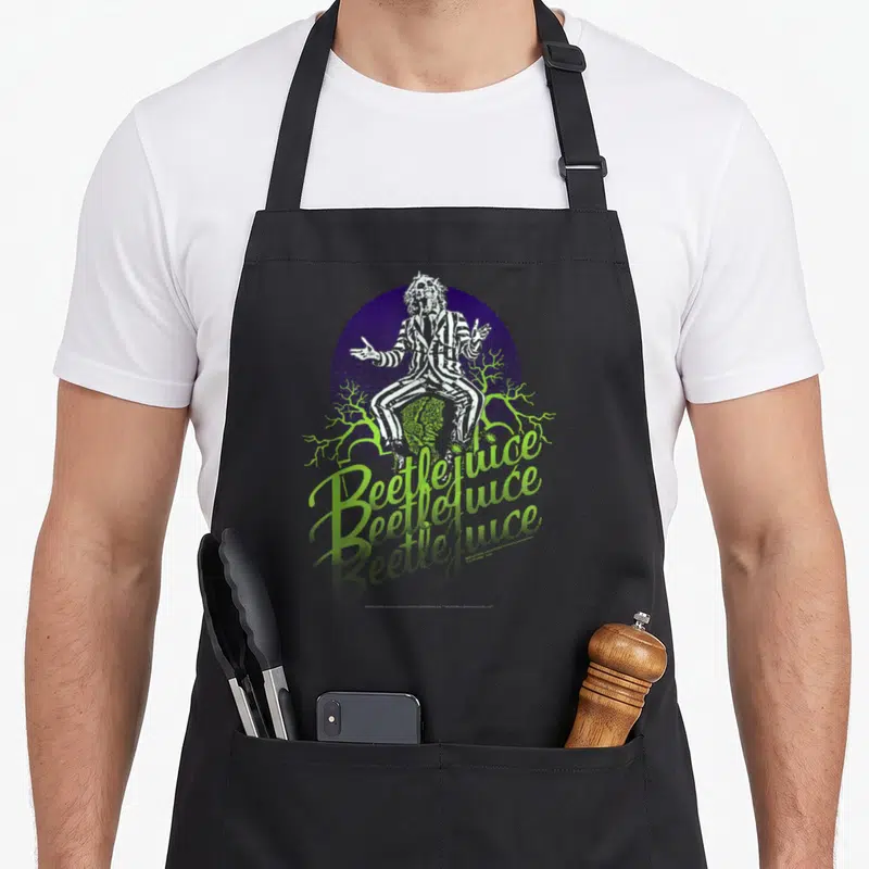Tablier de cuisine noir avec illustration Beetlejuice en costume rayé et texte vert fluo sur fond violet.