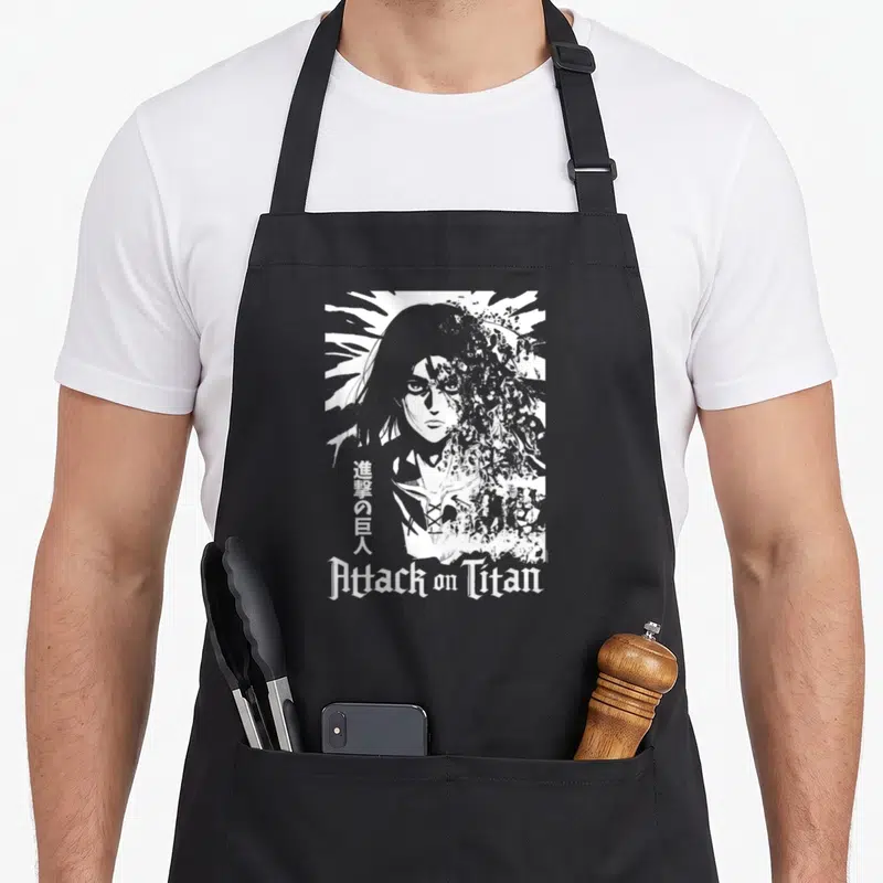 Tablier de cuisine noir avec illustration blanche d'Eren se désintégrant et le titre Attack on Titan en bas.