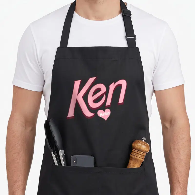Tablier de cuisine noir avec le mot Ken en rose et un petit cœur contenant Barbie