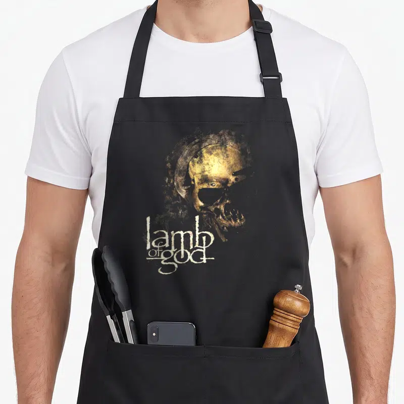 Tablier de cuisine noir avec un crâne doré et le texte Lamb of God en blanc stylisé.