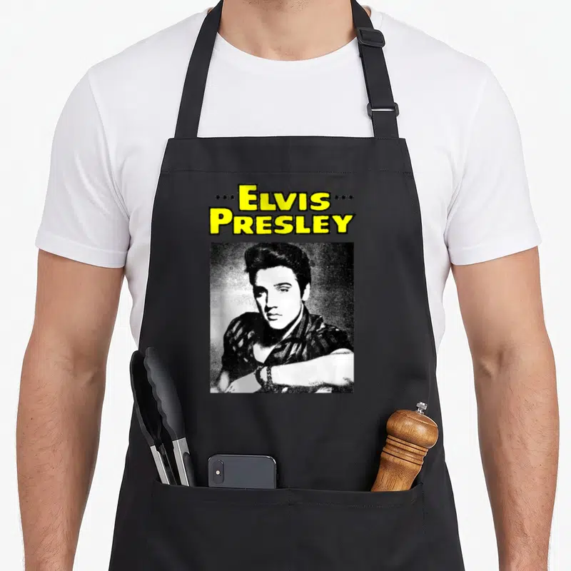 Tablier de cuisine noir avec portrait Elvis Presley et texte jaune Elvis Presley encadré de stars.