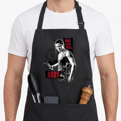 Tablier de cuisine noir avec illustration d'Abby tenant un marteau et le texte Bare Your Fangs en rouge.