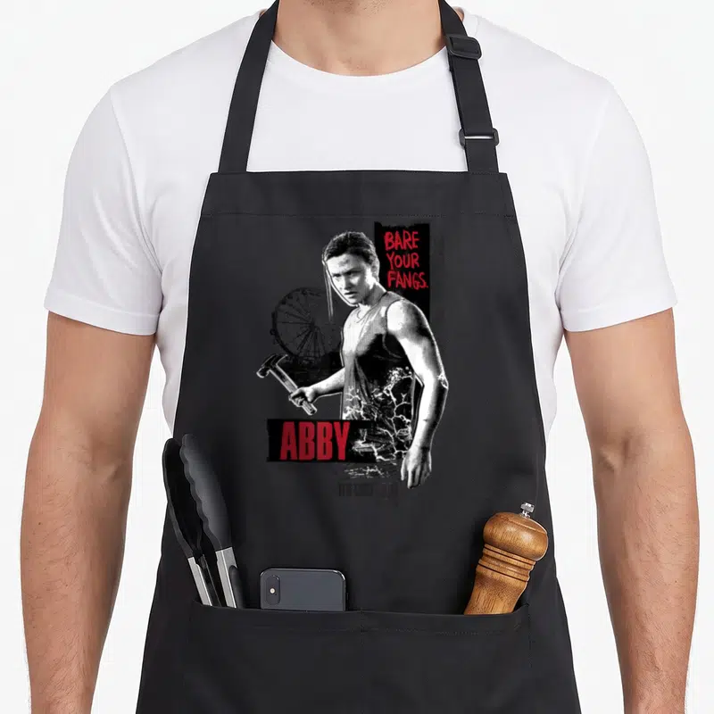 Tablier de cuisine noir avec illustration d'Abby tenant un marteau et le texte Bare Your Fangs en rouge.