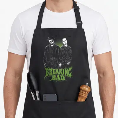 Tablier de cuisine noir avec illustration blanche de deux personnages et le texte BREAKING BAD vert en bas.