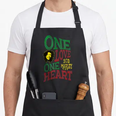 Tablier de cuisine noir avec l'inscription One Love One Heart et un portrait de Bob Marley aux couleurs du drapeau jamaïcain.