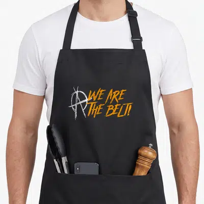 Tablier de cuisine noir avec le logo blanc et l'inscription orange We Are The Belt.