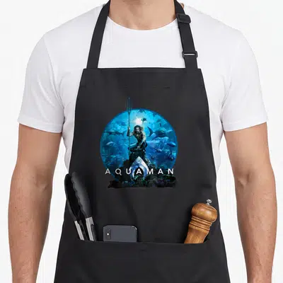 Tablier de cuisine noir avec illustration circulaire d'Aquaman tenant un trident au milieu de requins sous-marins.