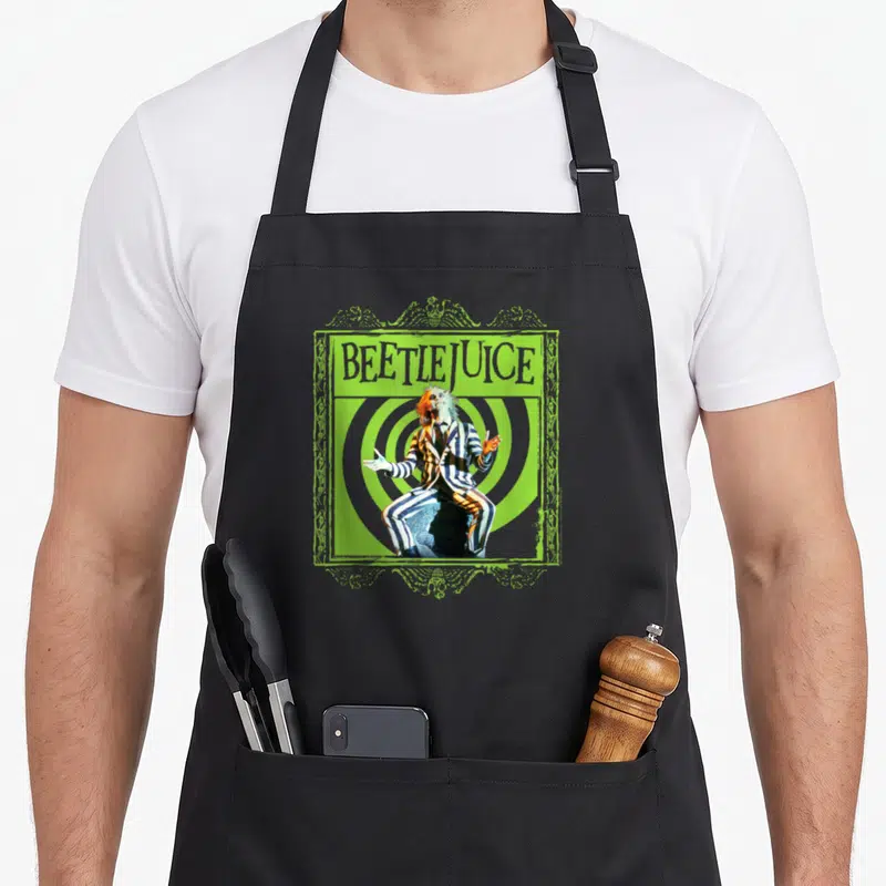 Tablier de cuisine noir avec illustration Beetlejuice en costume rayé sur fond de spirales vertes.