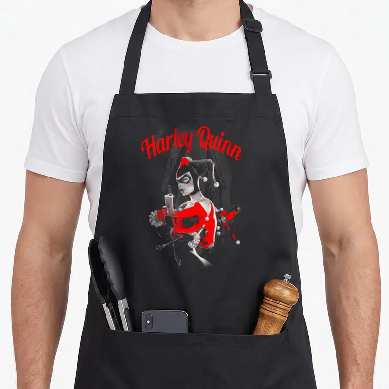 Tablier de cuisine noir avec illustration Harley Quinn Spring Gun en rouge et blanc tenant une seringue.
