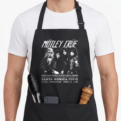 Tablier de cuisine noir avec l'inscription Mötley Crüe et quatre personnages au style hard rock en blanc sur fond sombre.