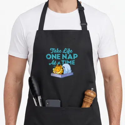 Tablier de cuisine noir avec Garfield dormant et la phrase Take Life One Nap At a Time en typographie bleue.