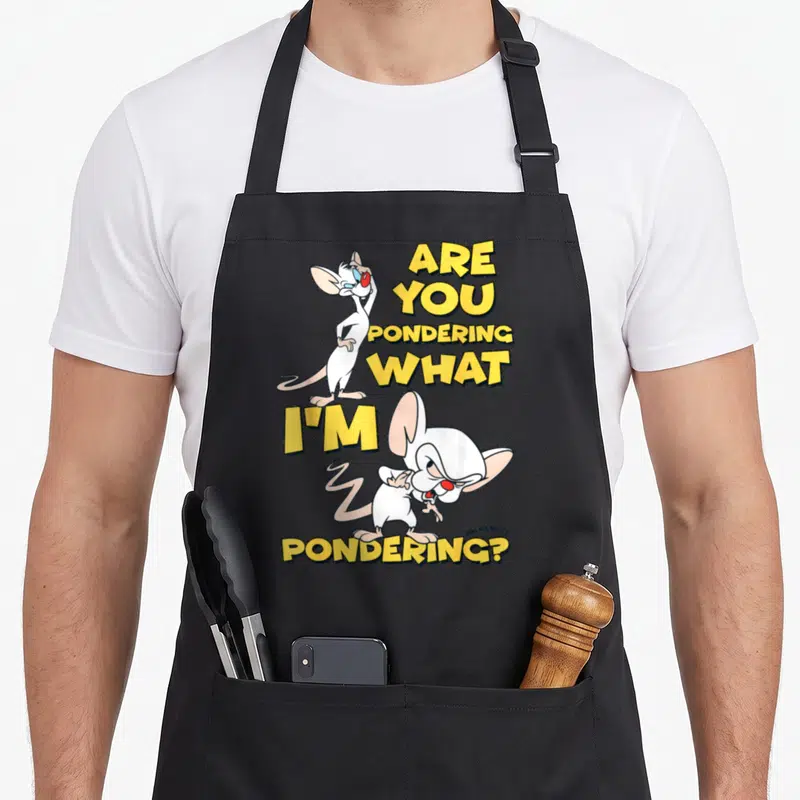 Tablier de cuisine noir avec l'illustration de Pinky et le Brain et le texte Are You Pondering What I'm Pondering en lettres jaunes.