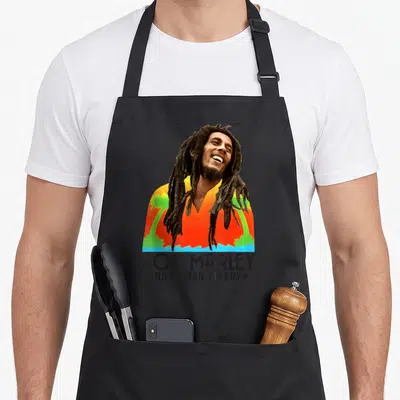 Tablier de cuisine noir avec portrait coloré de Bob Marley et texte No Woman No Cry en bas.