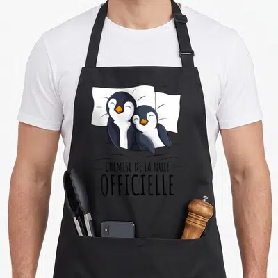 Tablier de cuisine noir avec deux pingouins au lit et le texte Chemise de la nuit.