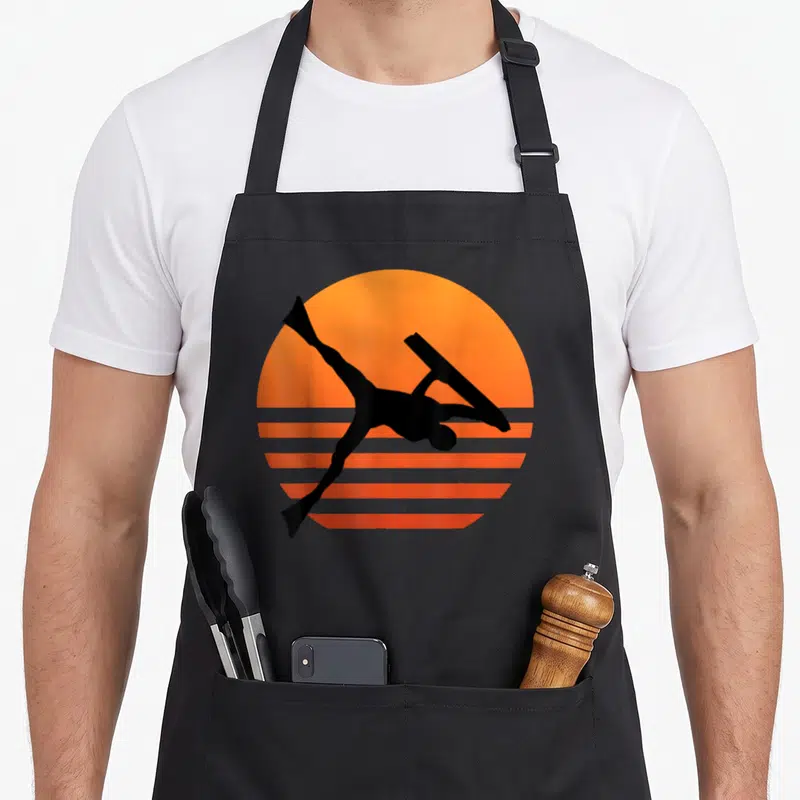 Tablier de cuisine noir avec silhouette bodyboarder air inverti sur soleil orange strié style rétro
