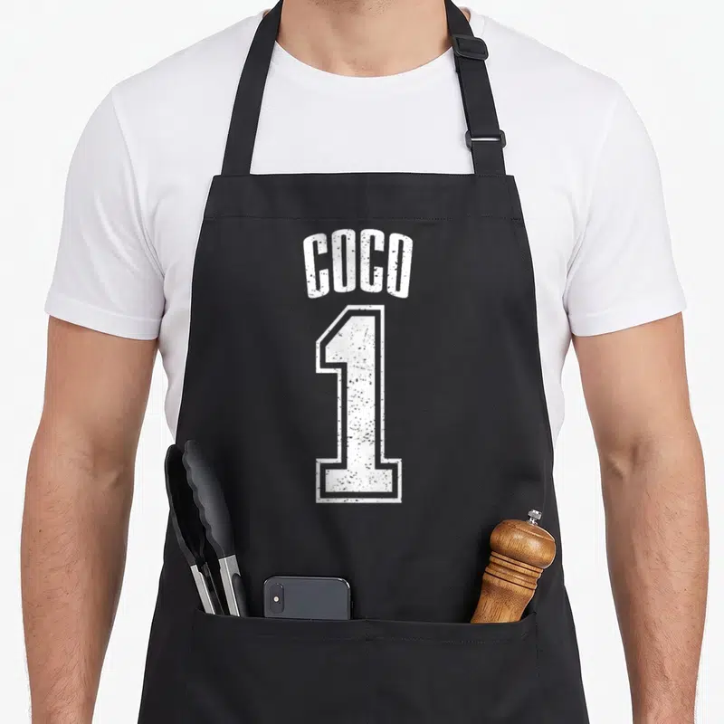 Tablier de cuisine noir avec l inscription Coco et le chiffre 1 en typographie blanche style maillot sportif dégradé.