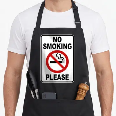 Tablier de cuisine noir avec un panneau blanc No Smoking Please barré en rouge au centre.