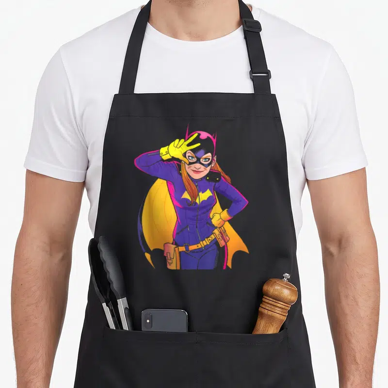 Tablier de cuisine noir avec illustration colorée de Batgirl Moves en train de faire un signe de la main.