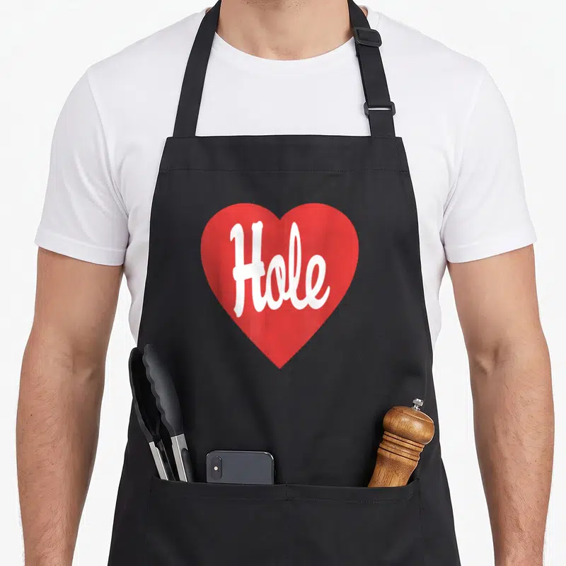 Tablier de cuisine noir avec un grand cœur rouge affichant le mot Hole en écriture cursive blanche au centre.
