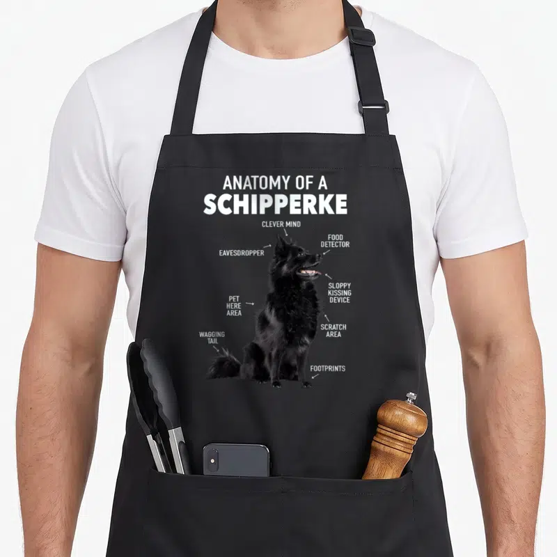Tablier de cuisine noir avec illustration anatomique humoristique d'un chien Schipperke noir assis.