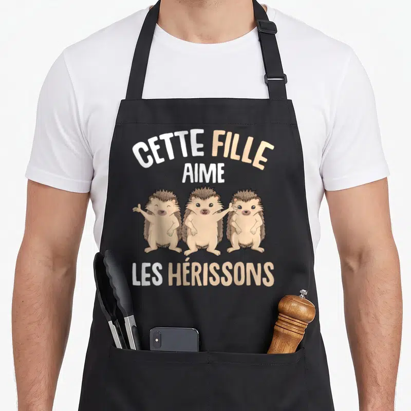 Tablier de cuisine noir avec trois hérissons souriants et le texte Cette Fille Aime Les Hérissons imprimé en blanc et beige.